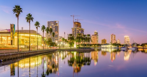 Skyline of St. Petersburg in Florida during sunset in front of palm trees and a harbor.