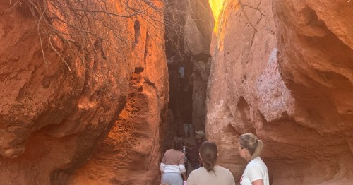 A group of hikers look into a narrow slot canyon in southern Utah.