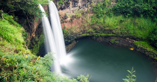 Wailua Falls on Kauaʻi, a 173-foot double waterfall plunging into a lush tropical pool surrounded by greenery.