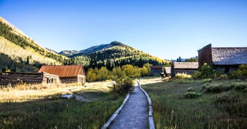 A scenic path leading through Ashcroft, a ghost town in Colorado, surrounded by mountains and trees under a clear sky.
