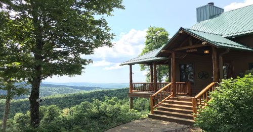a wooden cabin with a green roof and stairs atop a grassy hill in the forest in arkansas