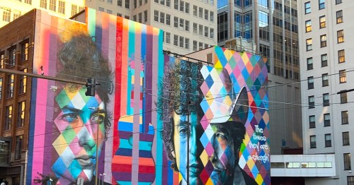 A large, colorful Bob Dylan mural featuring geometric patterns and a guitar on a building in Minneapolis, MN.