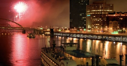 * Fireworks light up the night sky over the Gateway Clipper Fleet in Pittsburgh, with city buildings reflecting in the water.