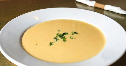 * Creamy Beer Cheddar Soup served in a classic white bowl, placed on a rustic wooden table.