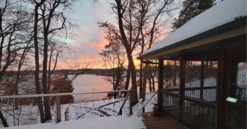 The winter sun glows on the horizon and over a frigid lake, as seen from a snow-covered deck at a rental property in Minnesota.