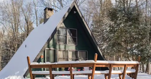 A deck covered in snow sits in front of a snow-capped A-Frame Airbnb in Pocono Pines, Pennsylvania.