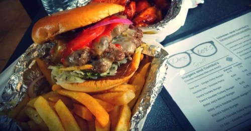 A combo meal featuring a loaded double cheeseburger and french fries displayed in foil wrappers alongside a menu for Dexter's Grill.