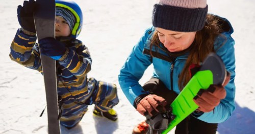 A woman and a child stand together, each holding a pair of skis, ready for a day on the slopes.