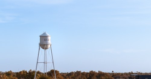 a water tower that says "GILBERT" on it with trees in the back and a pale blue sky