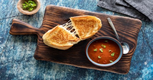 Top down view of a grilled cheese sandwich with tomato soup on a wooden board