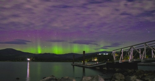 green and purple sky lit up by the northern lights in front of a body of water in idaho