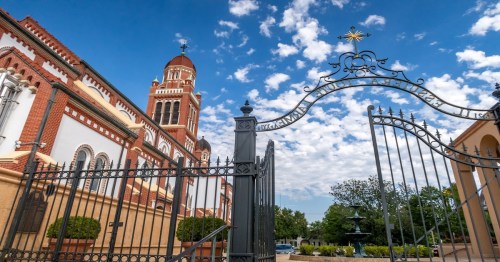 cathedral enclosed with rot iron gates with a partly cloudy sky above in lafayette