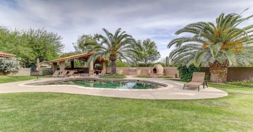 view of palm trees and a pool near grass and cloudy skies in a luxury airbnb in arizona