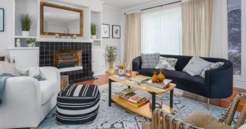 Interior of a living room with white walls, tan curtains, grey and white patterned rug, cough and cozy chair.