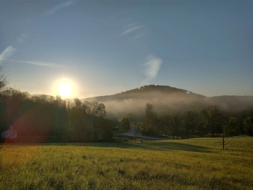 A sun sets over a large hill and forest as mist rises from Mohican State Park in Ohio.