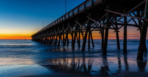 a pier on myrtle beach with the ocean underneath and a golden and blue sky in the background during sunset in south carolina