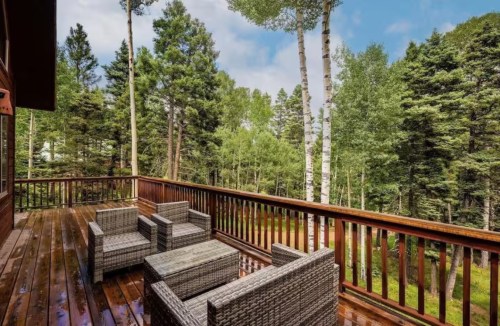 outdoor table and chairs on a wraparound deck with trees nearby at a nex mexico winter cabin