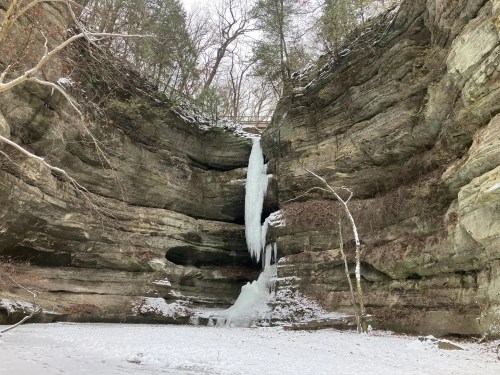 A sandstone cliff is surrounded by snow and dripping with naturally-formed ice sculptures.