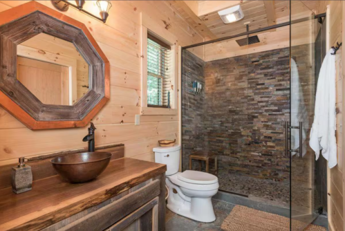 A luxury cabin bathroom, set up with a bronze sink and large mirror, dazzles visitors with its stone walk-in shower.
