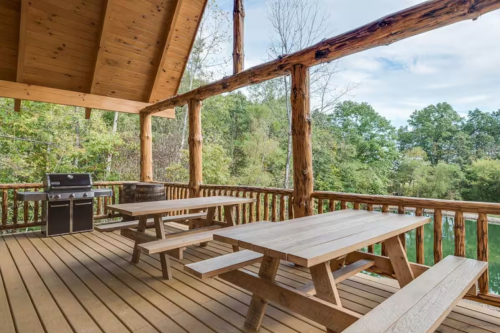 A wooden deck with two tables and a grill looks over a forest-surrounded lake in West Lafayette, Ohio.
