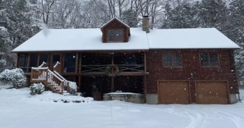 A cozy, two-story wooden lodge covered in fresh snow with a festive wreath hanging on the balcony.