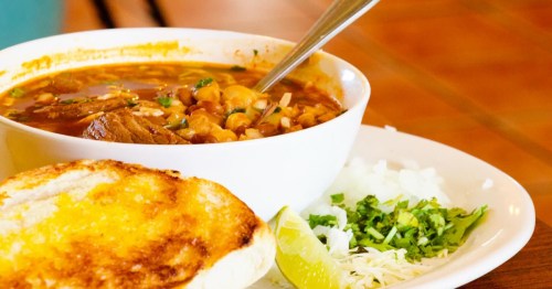closeup of a bowl of soup in a white bowl on top of a white plate with toast