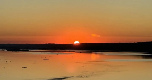 An orange sunset over a vast lake in Illinois reflects across the still water.