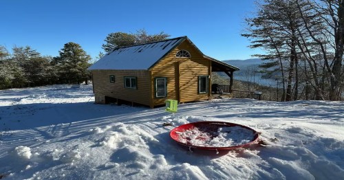 Winter cabin in Tennessee seated in the middle of snowy grounds and winter trees.