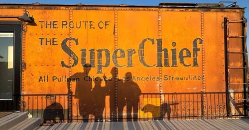 the shadows of a family and two dogs on an orange colored pullman train car turned airbnb in texas
