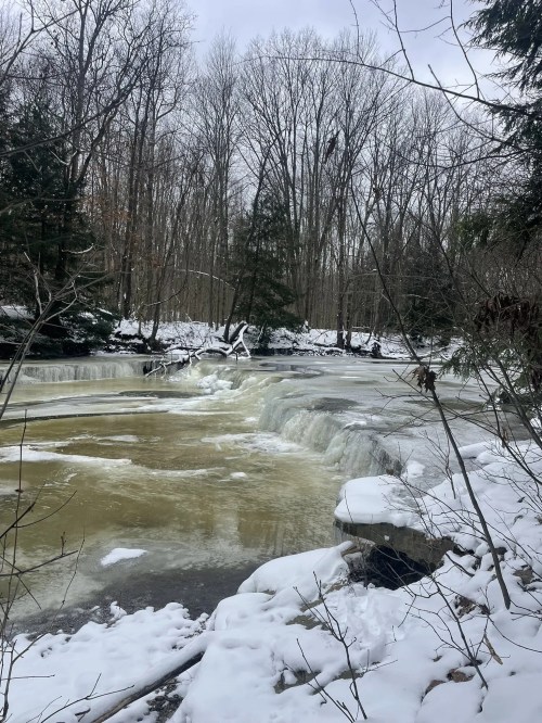 A snowy, wintry scene surrounds a waterfall flowing through an Ohio creek.