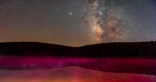 Night dark sky with milky way galaxy in Spruce Knob Lake in West Virginia with red pink color water reflection from flashlight on fog mist rising steam