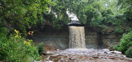 In the depths of summer, a waterfall beneath a bridge trickles into a foliage-framed waterway in Wisconsin.