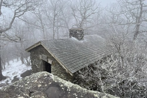 A stone Appalachian Trail shelter on a wintery day with fog rolling in swirling a mist of eerieness to this wintery scene.