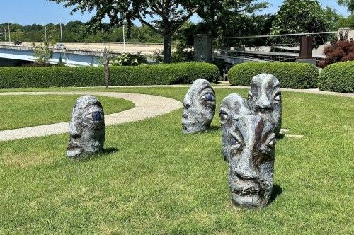 A paved path curves by these strange stone sculptures of human faces looking out towards those who walk by.