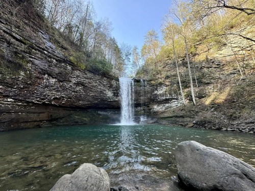 A bowl-shaped rock canyon with a waterfall plunging into the sparkling pool below.