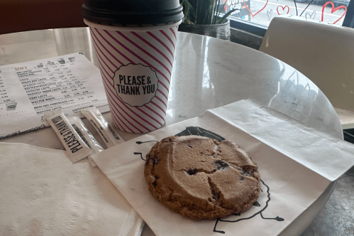Hot tea in a to-go cup and a chocolate chip cookie on parchment