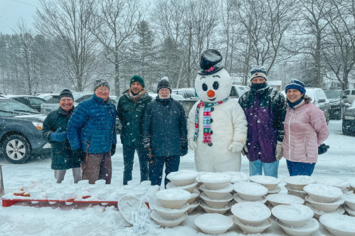 A group of six adults pose with a person dressed as a snowman in front of bowls of snow at the Brattleboro Winter Carnival in Brattleboro, Vermont.