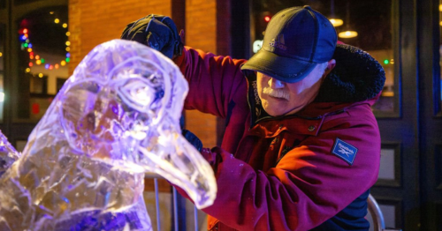 A man with a black hat and a red coat carves an ice sculpture of a bird at the Lowell Winterfest festival in Lowell, Massachusetts.