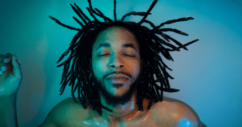 A man with his eyes closed peacefully floats on his back in a pool of water, his hair spread out around his face.