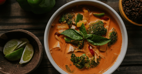A bowl is filled with a vibrant curry with broccoli and thai basil.
