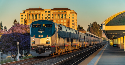 An Amtrak train pulls into a serene-looking train station at golden hour.