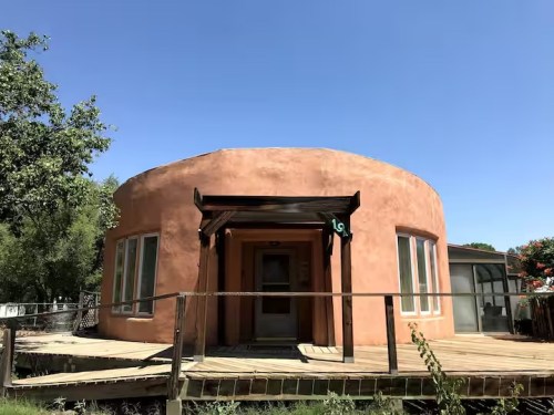 Unique Airbnb in Peralta, New Mexico, with a round adobe house and a rustic wooden deck.