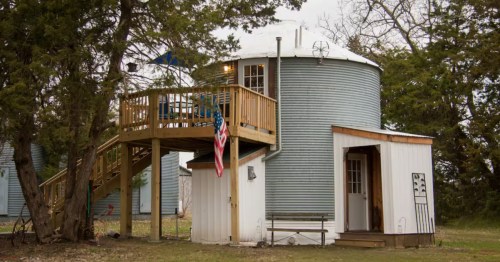 Exterior of Butler Grain Bin Airbnb, a converted metal silo guest house with a wood deck and stairs in Nebraska.