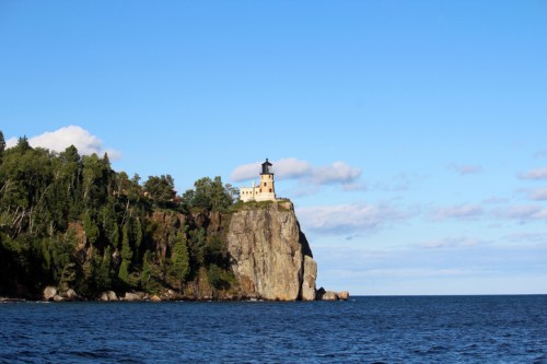 Beautiful view of the Split Rock Lighthouse towering high above Lake Superior on a cliff in Minnesota. Blue sky with fluffy purple clouds, brilliant blue water and dense forest. Travel. Nature.