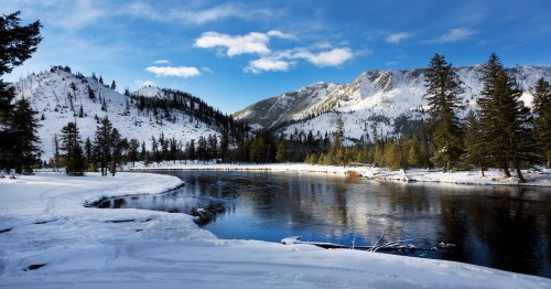 A view of the Yellowstone River by mountains covered in snow at Yellowstone National Park.