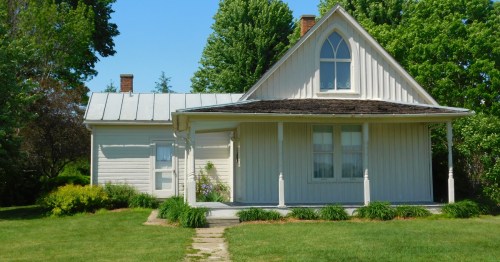 A white house with a prominent Gothic window stands on a lush green lawn under a clear blue sky.