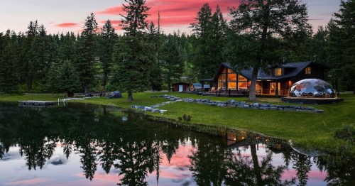 a cabin with situated under a pinky-blue sky, and forest trees with a lake in the front