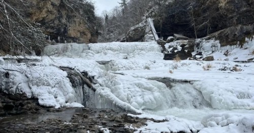 A small stream of flowing water can be seen among the ice formations of a frozen waterfall in limestone gorge.