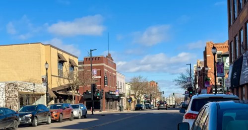 A sunny street view of downtown Hopkins, Minnesota, featuring classic storefronts, parked cars, and a clear blue sky.