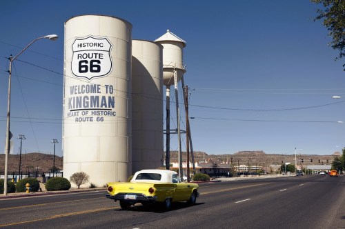 Large water towers on Route 66 in Kingman Arizona with a yellow and white classic car cruising by